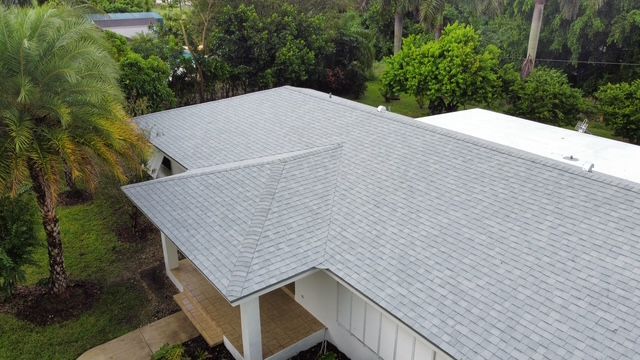 An aerial view of a house with a gray roof surrounded by palm trees.