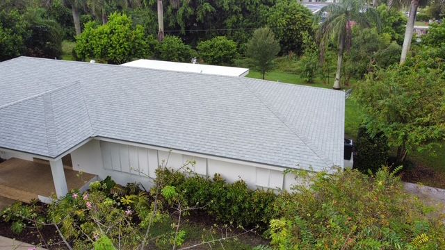 An aerial view of a house with a gray roof surrounded by trees and bushes.