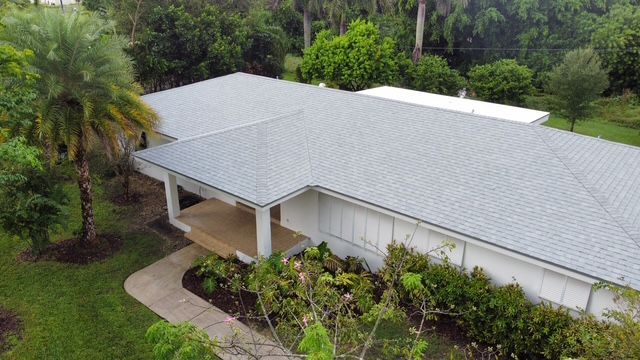 An aerial view of a house with a gray roof surrounded by trees.