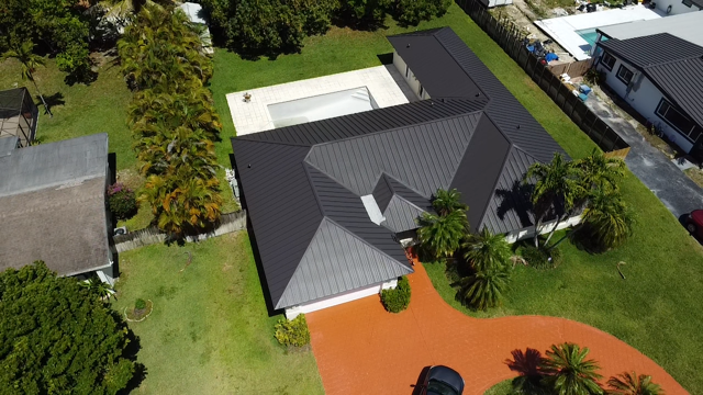 An aerial view of a house with a black roof and a pool.