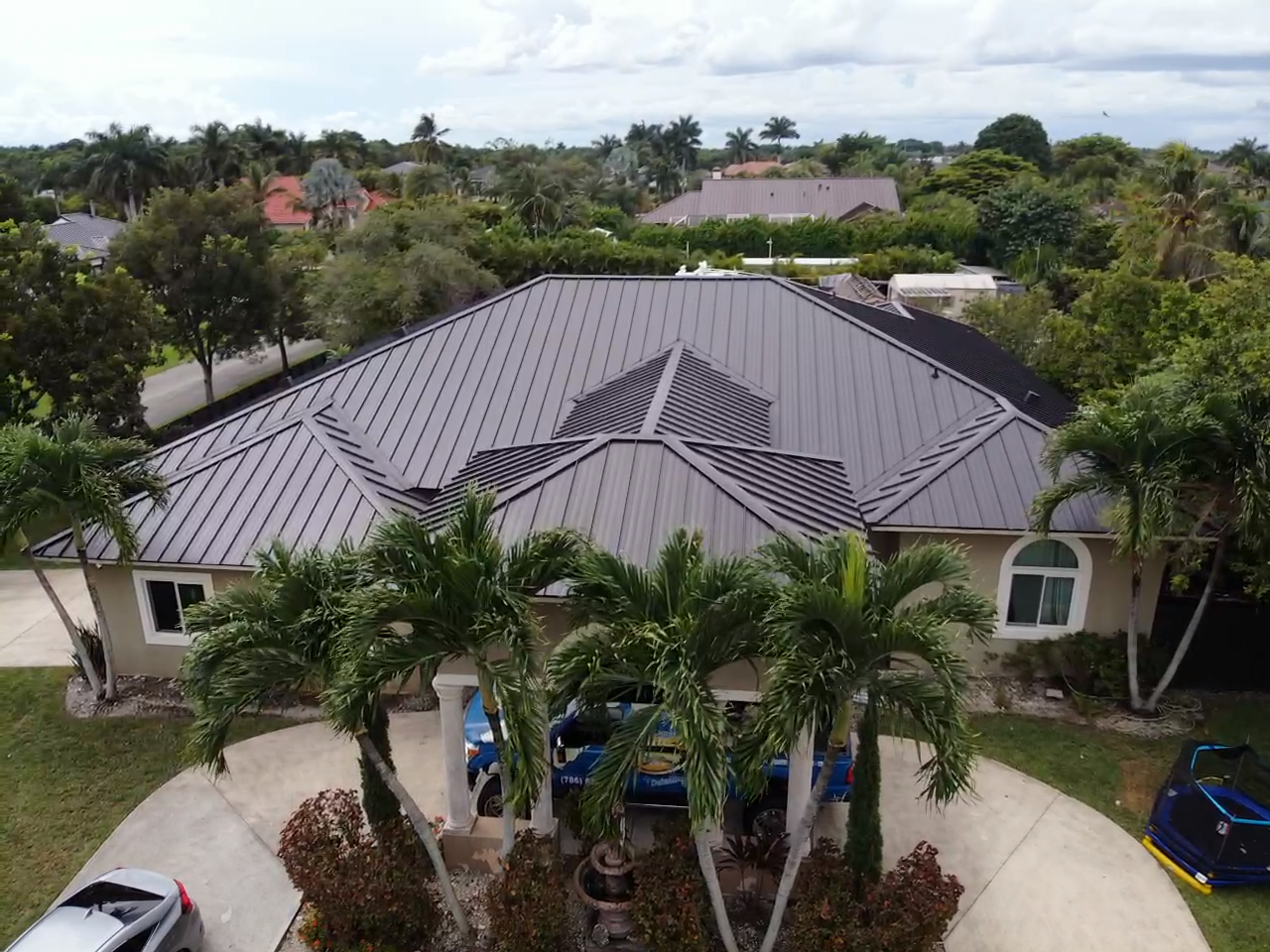 An aerial view of a house with a metal roof surrounded by palm trees.