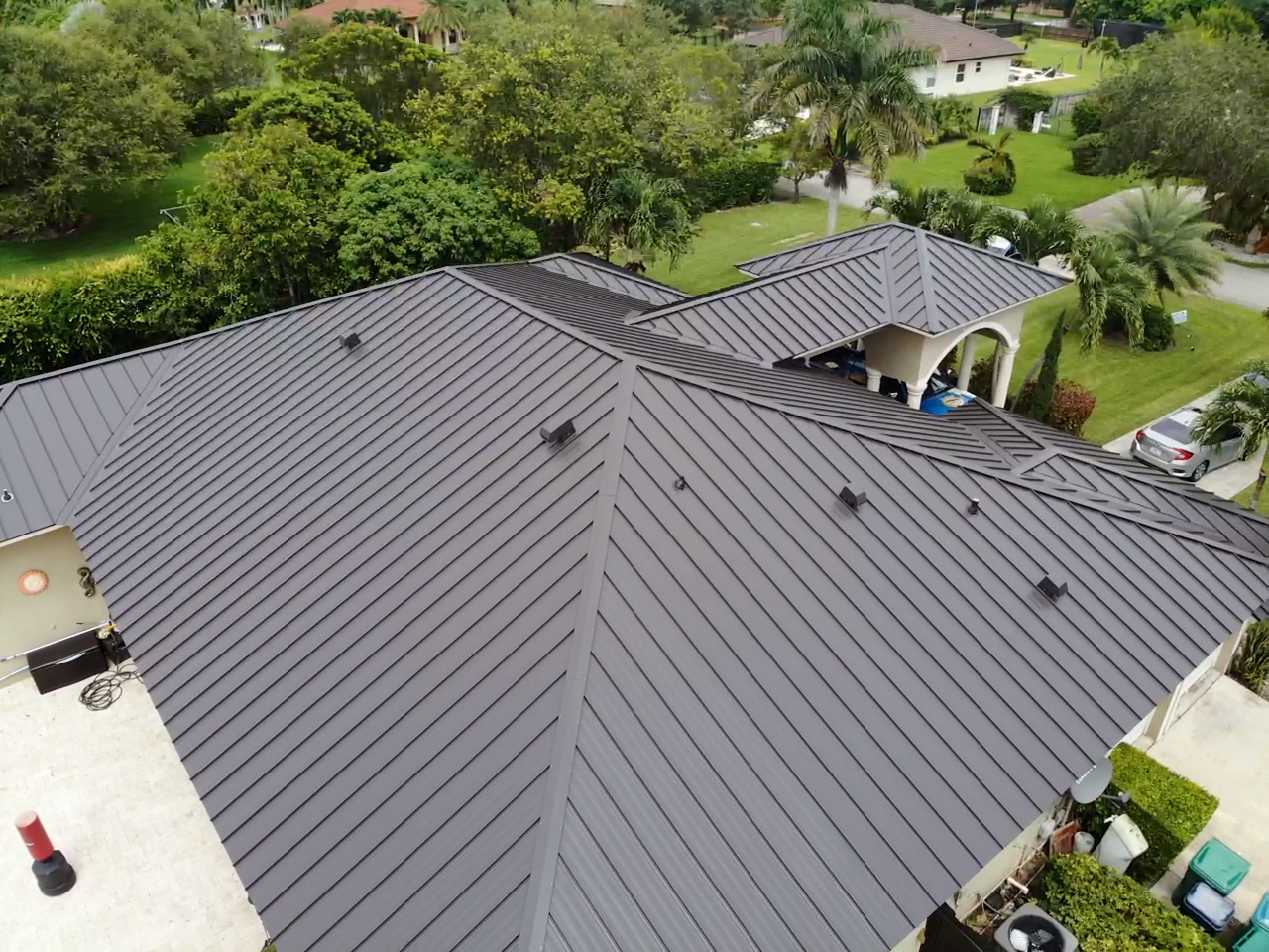 An aerial view of a house with a black roof surrounded by trees.