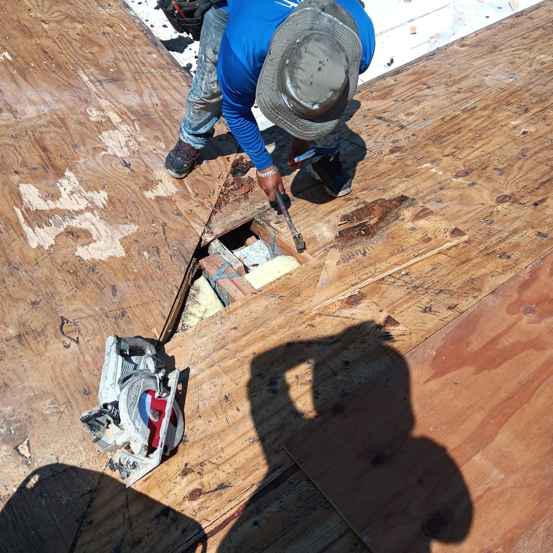 A man wearing a hat is working on a wooden roof.