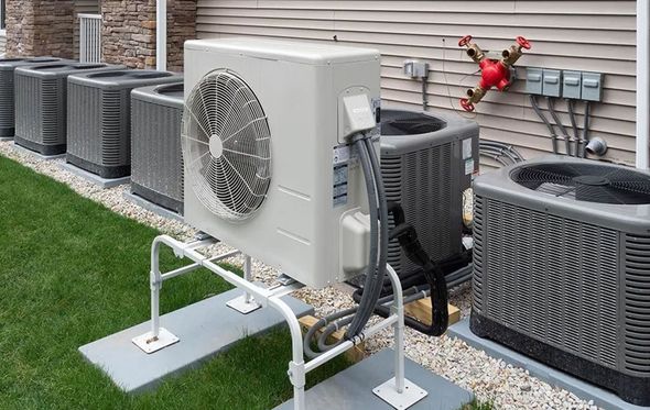 Outdoor air conditioning units lined up on a grassy lawn next to a building.