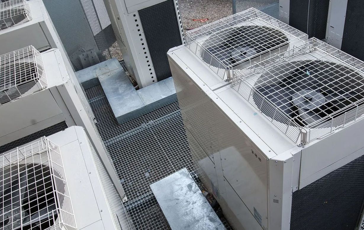 Air conditioning units on a rooftop, with metal grates and a gray/white color scheme.