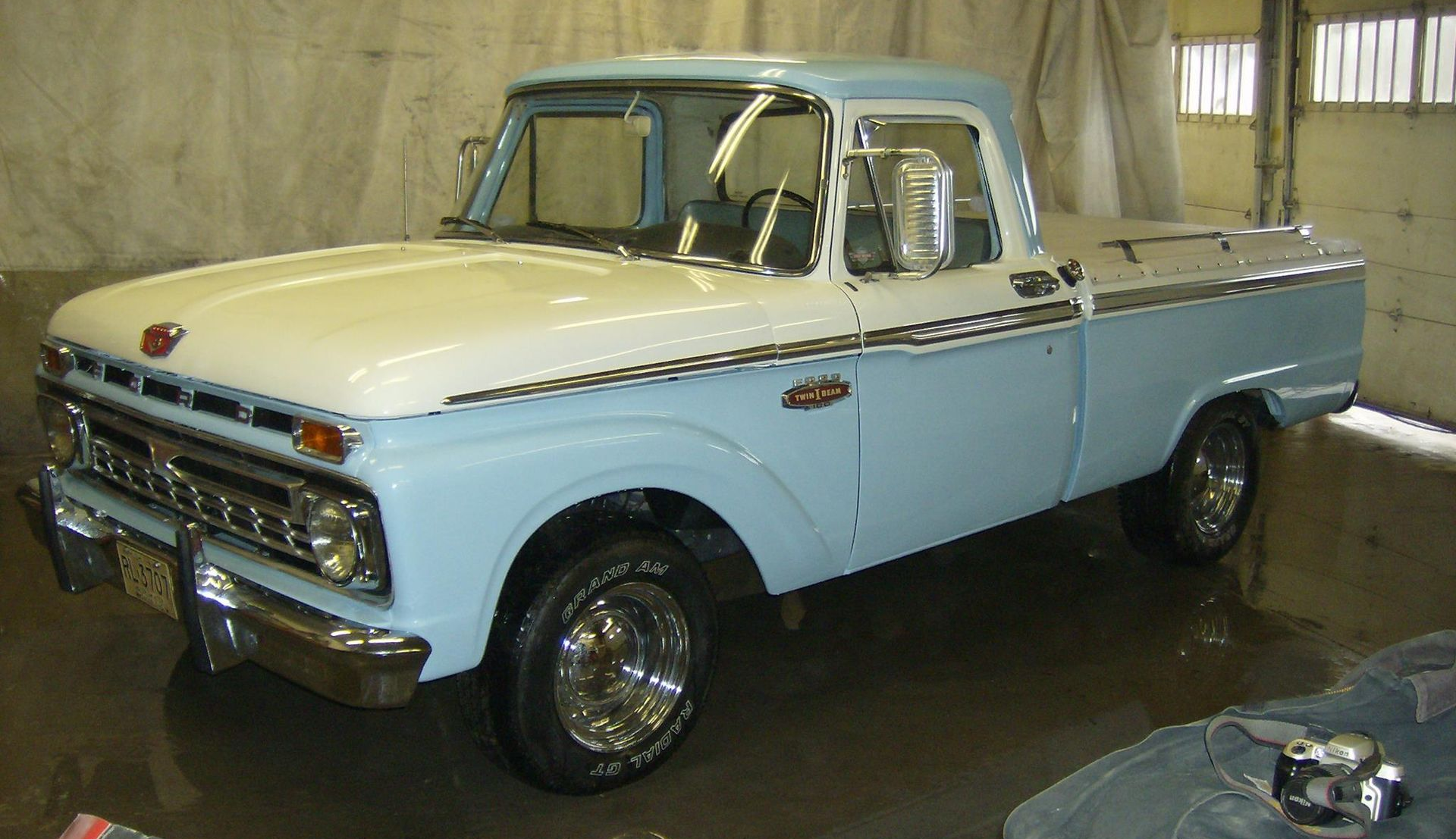 Two-tone light blue and white vintage Ford pickup truck parked inside a garage.