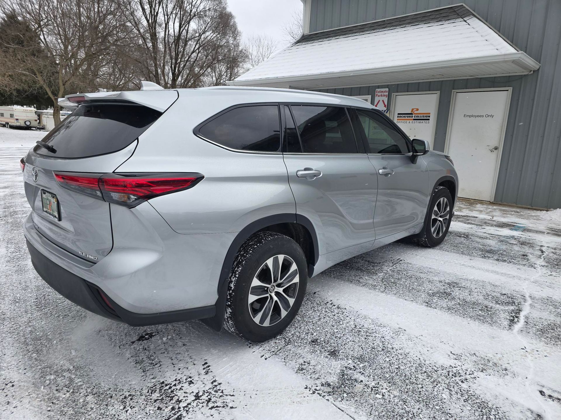 A silver SUV parked in a snowy parking lot next to a grey building.