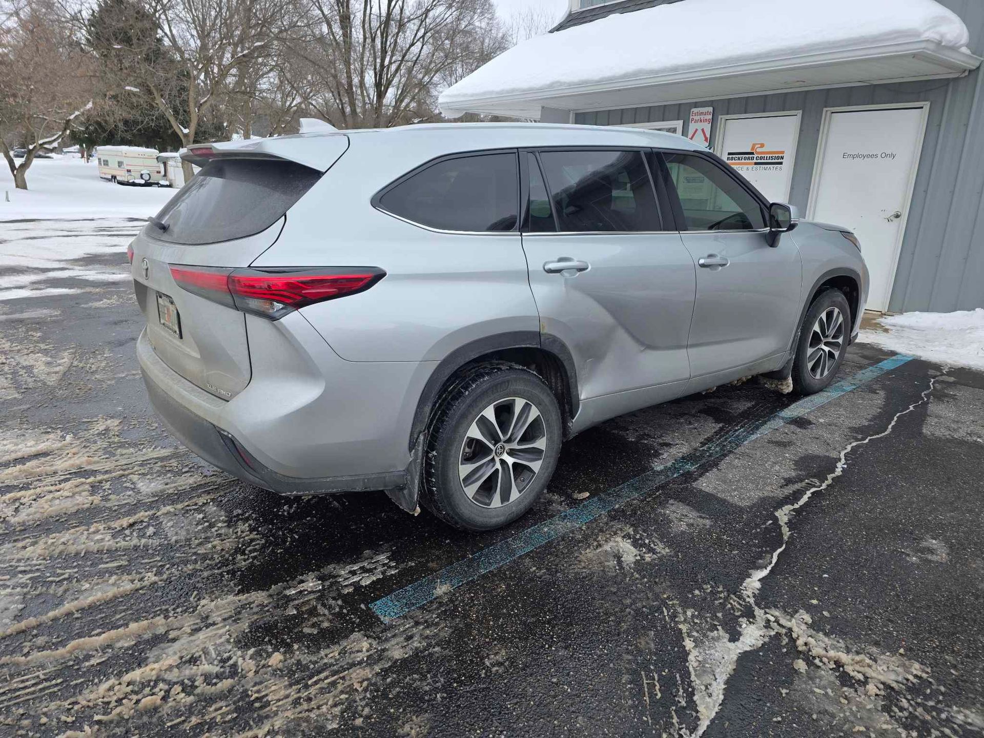 A silver SUV parked in a snowy parking lot next to a building.