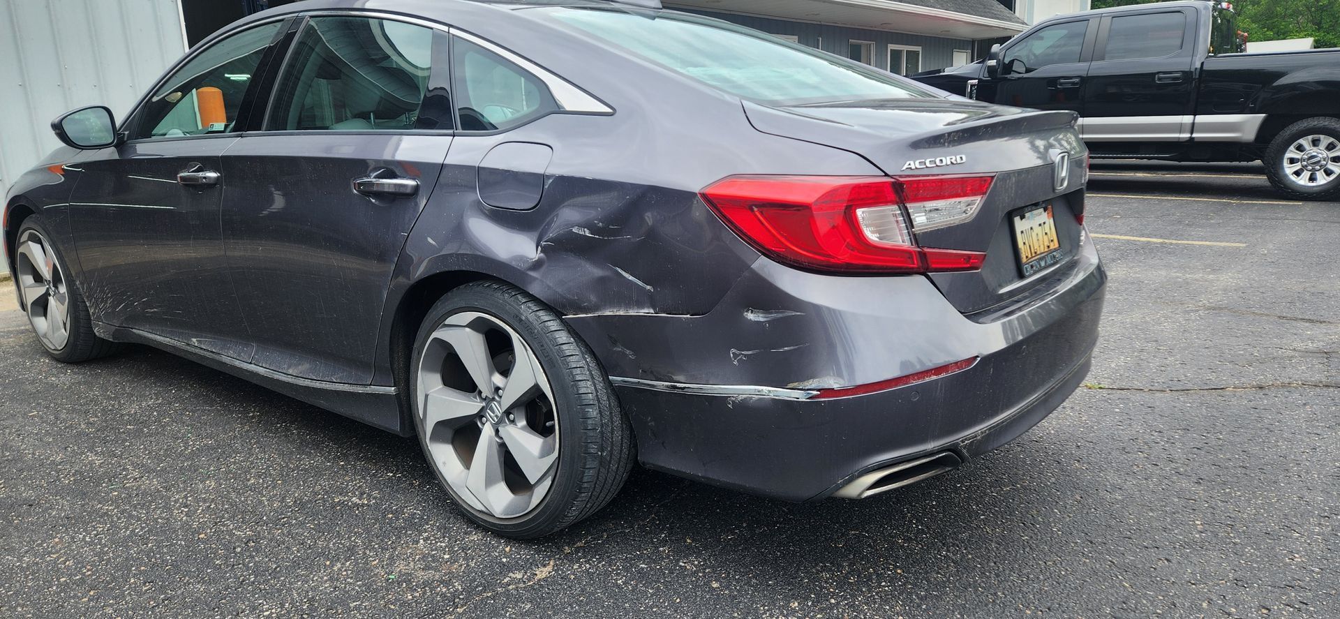 Gray Honda Accord car with damage on the side, parked on asphalt. A black pickup truck is in the background.