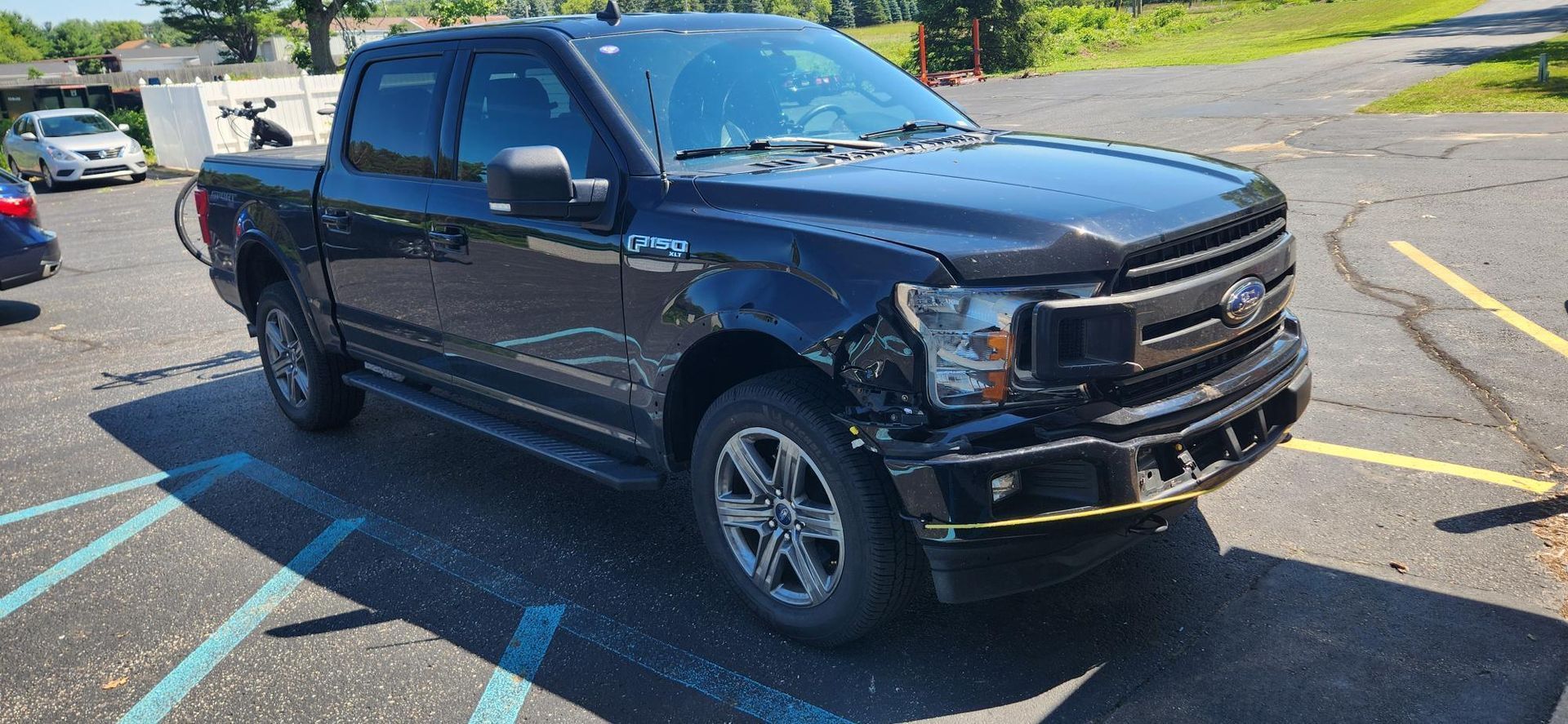 Black Ford F-150 pickup truck with front-end damage parked in a parking lot.