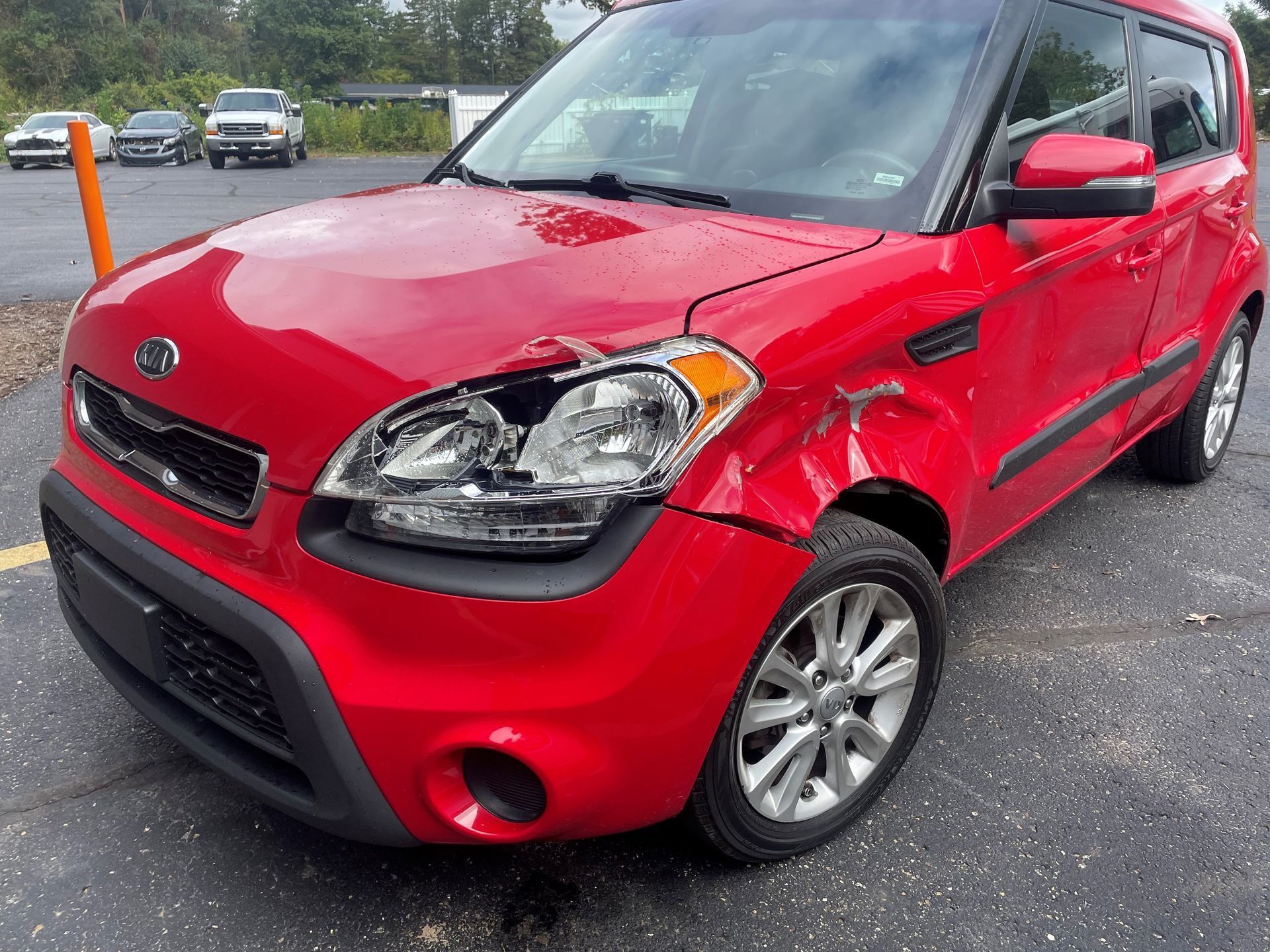 Red Kia Soul with front-end damage parked on asphalt.