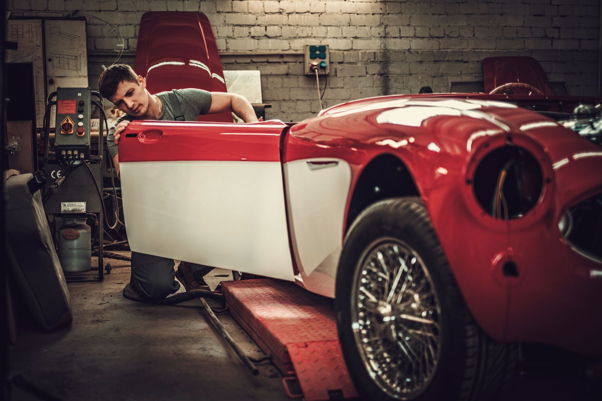 Man working on a classic red and white car in a garage.