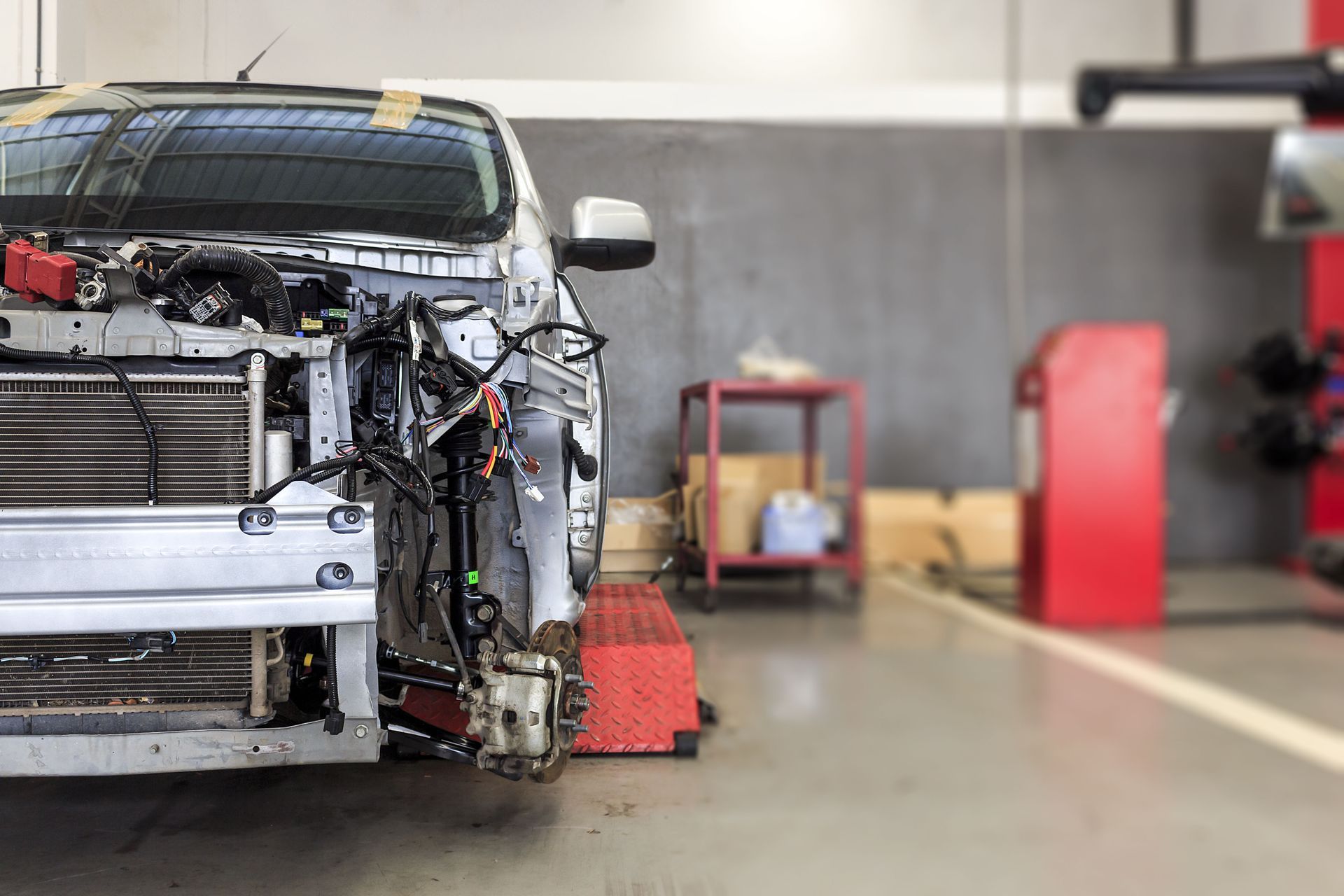 Damaged car in a repair shop with front-end components removed, focus on exposed engine parts and radiator.