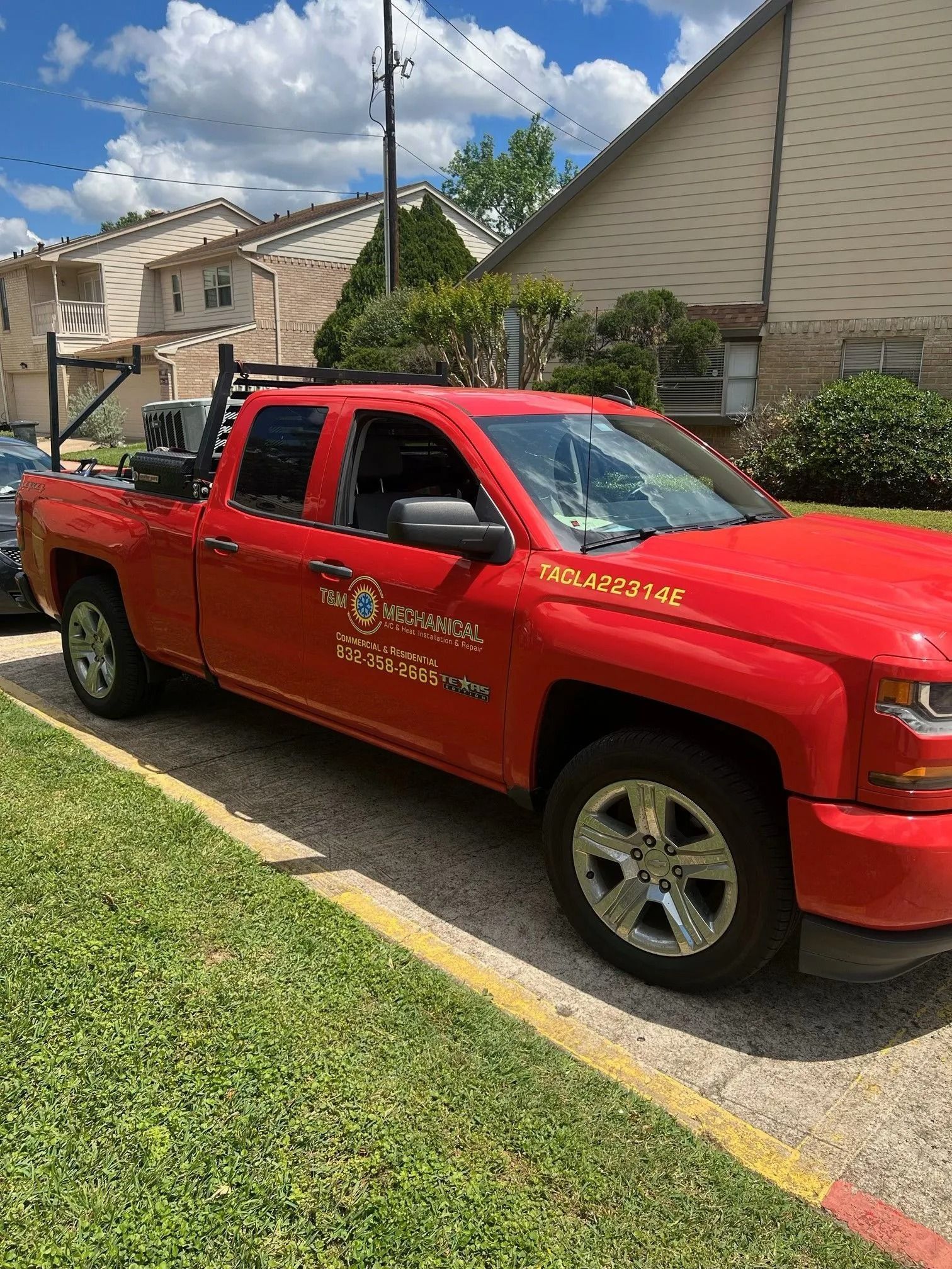 Red pickup truck parked on the side of a road, next to a grassy area. It has a ladder rack and company logo on the side.