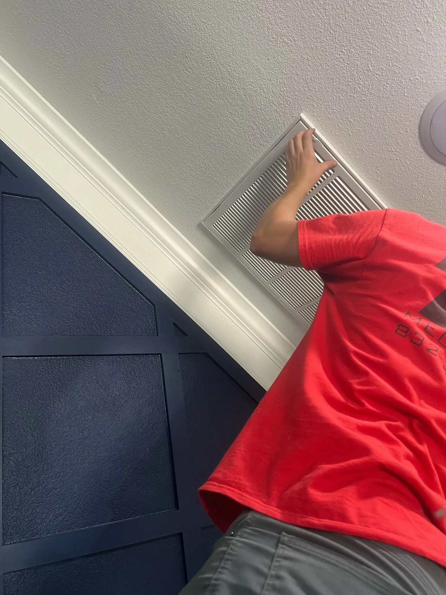 Person in red shirt installing a vent in a room with blue paneled wall and white trim.