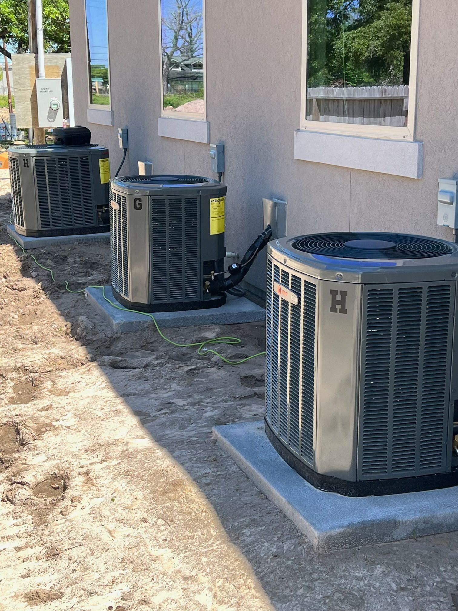 Three air conditioning units on concrete pads beside a building.