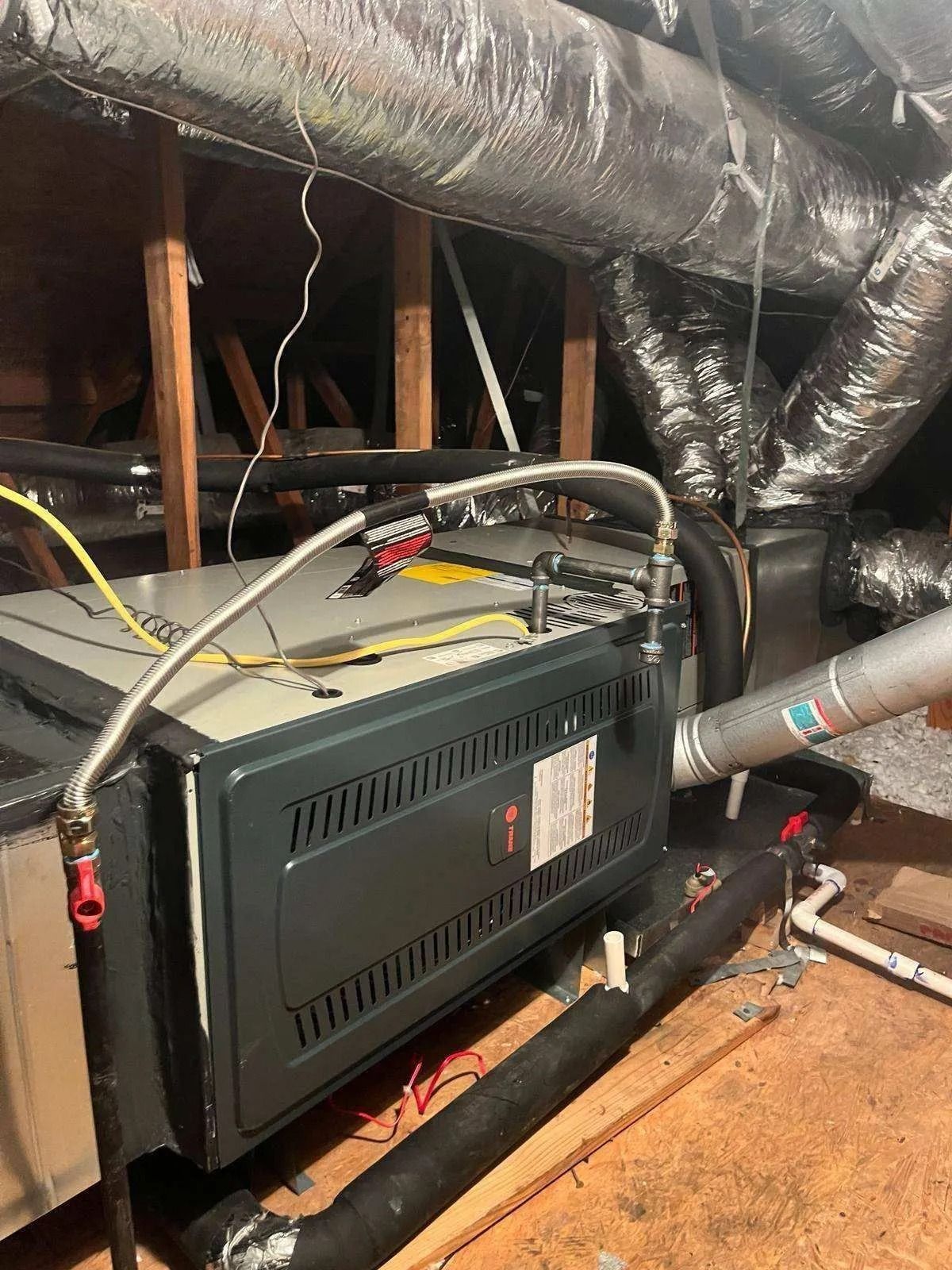 Furnace in an attic with ductwork and gas line.