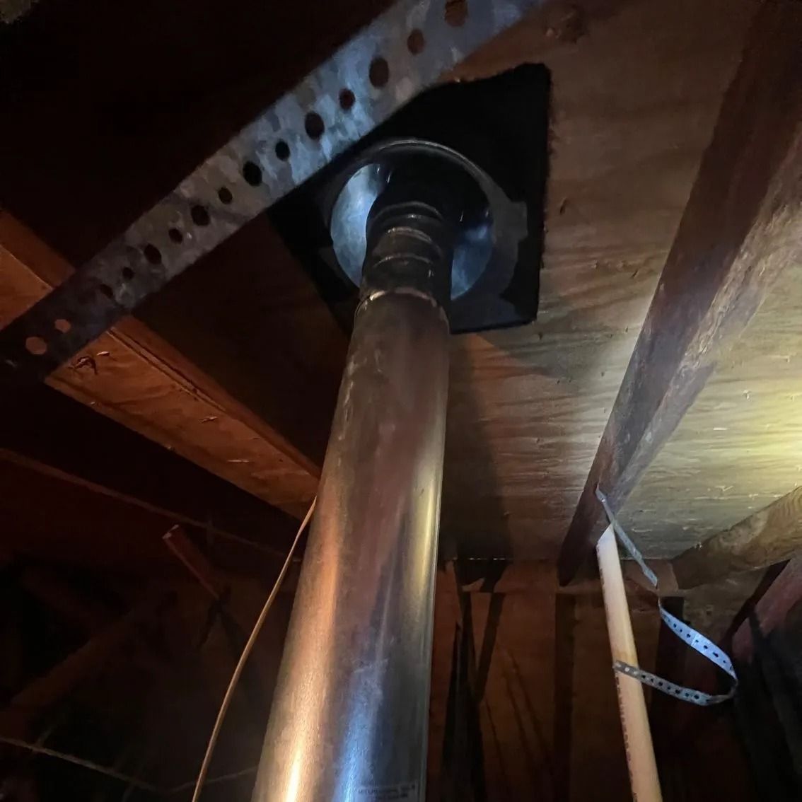 Metal chimney pipe passing through a wooden ceiling with a metal bracket and other wooden supports.