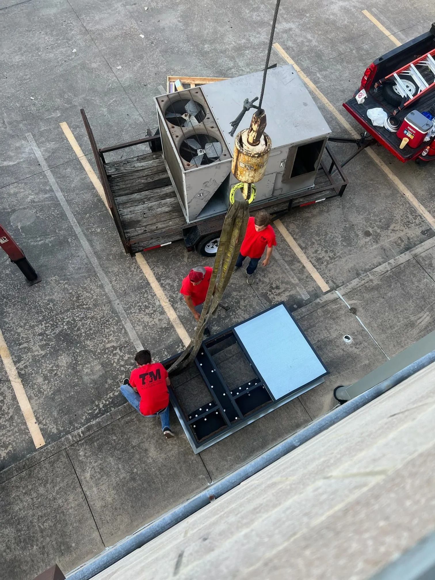 Workers using a crane to lift an HVAC unit on a rooftop.