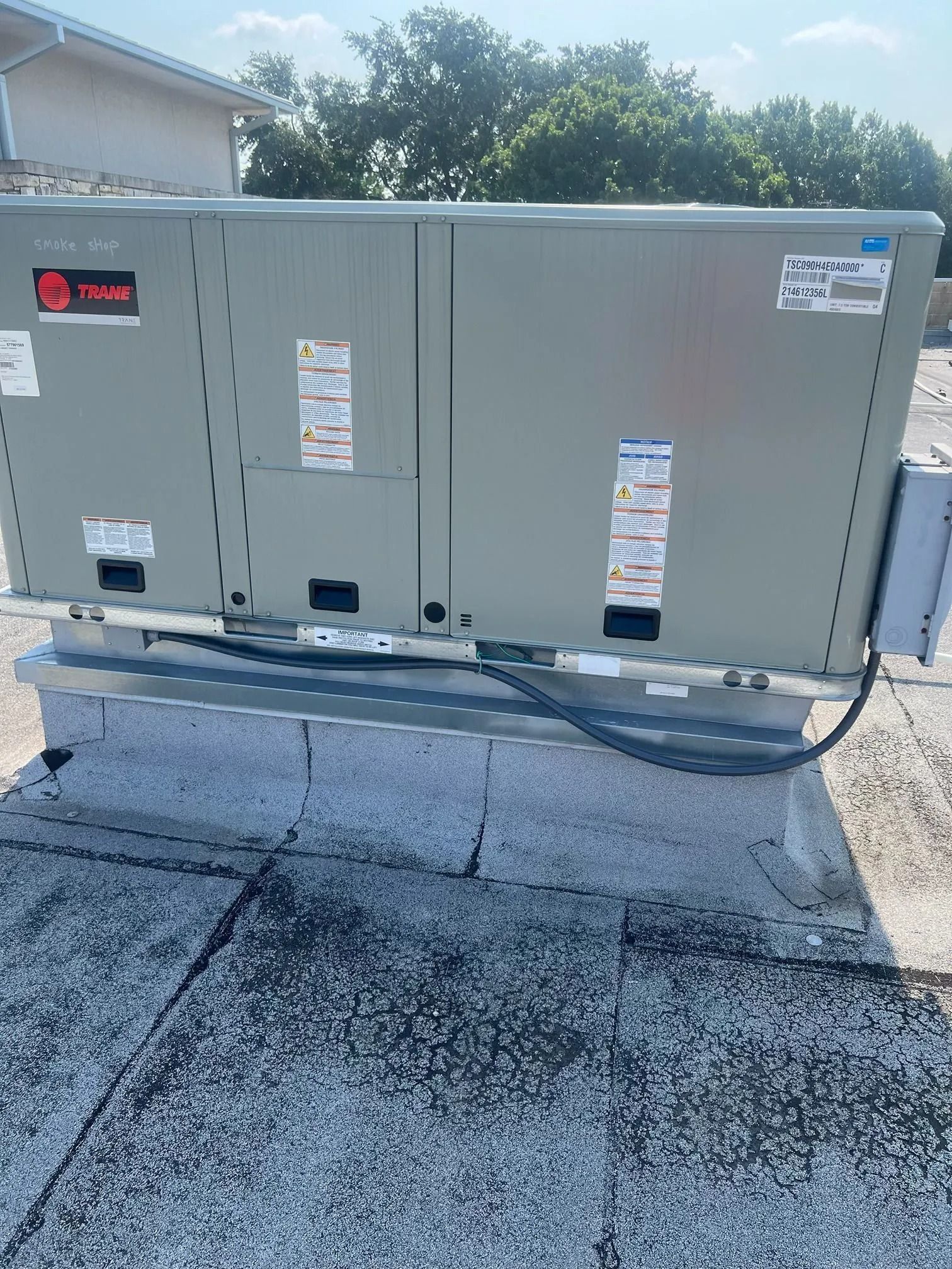 Gray HVAC unit on a rooftop, with labels and a black cable.