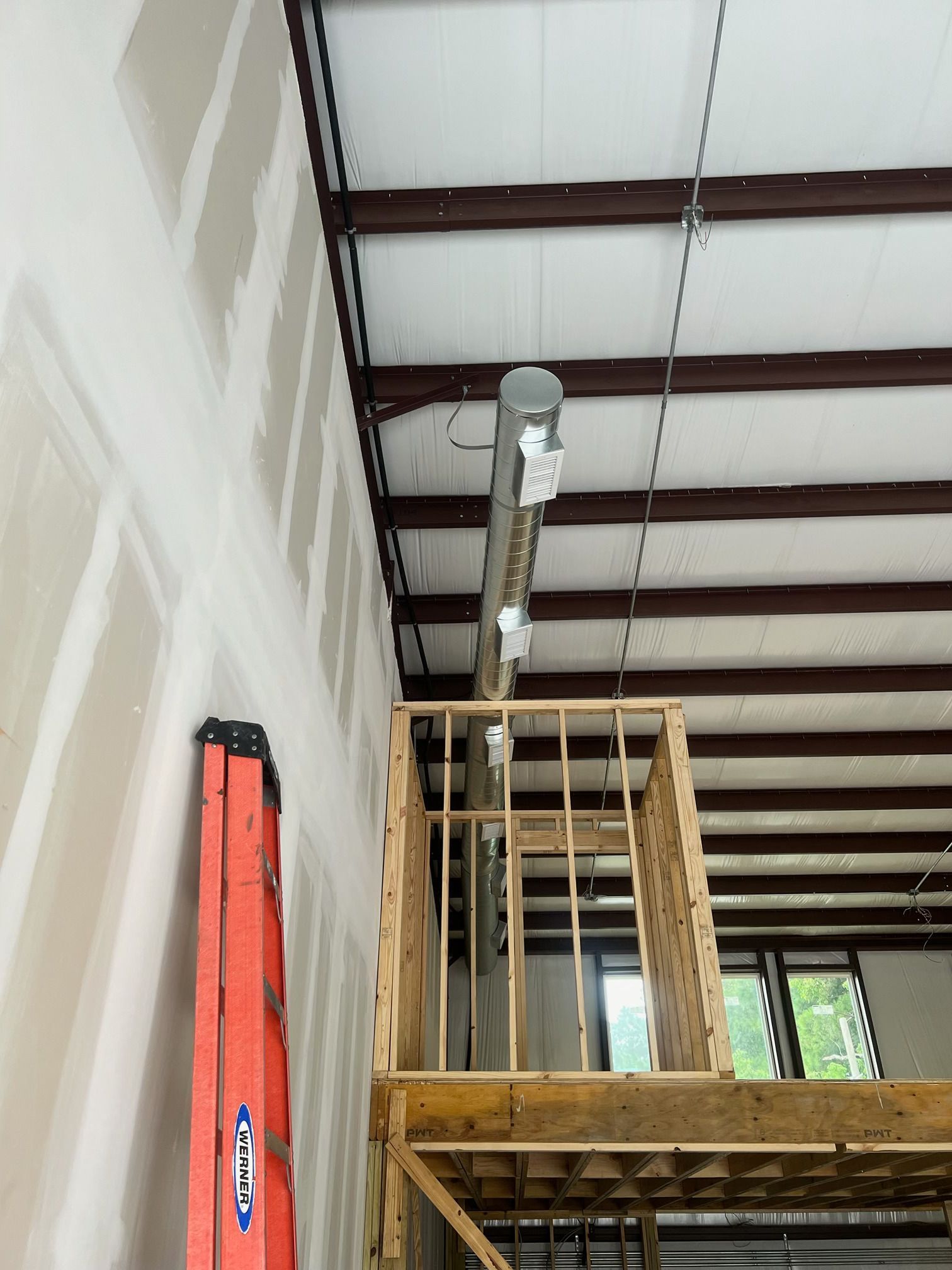 Orange ladder against a drywall wall, with a small wooden structure extending from a mezzanine.