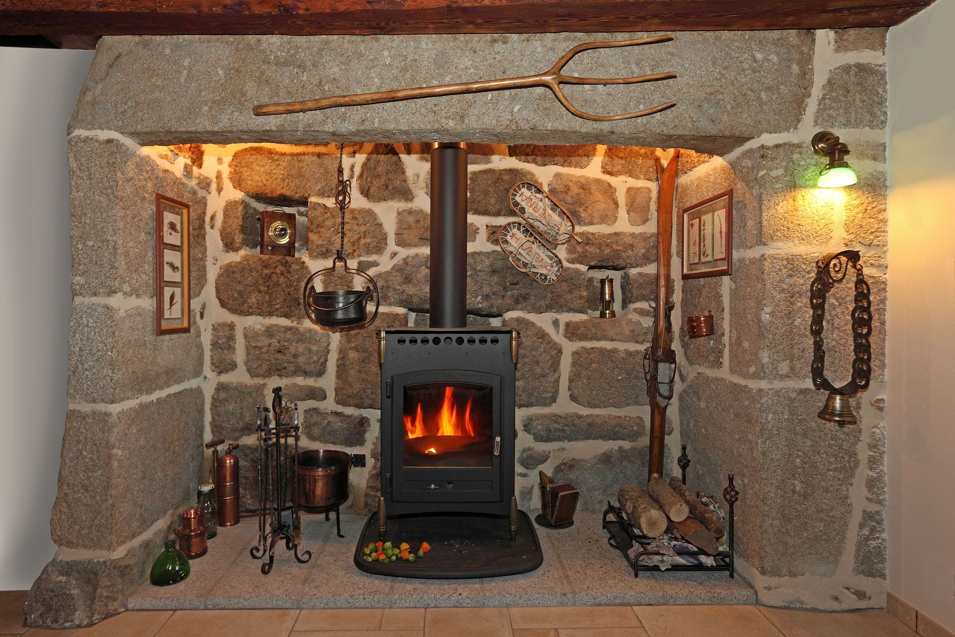 Stone fireplace with a wood-burning stove, rustic decor, and a pitchfork above.