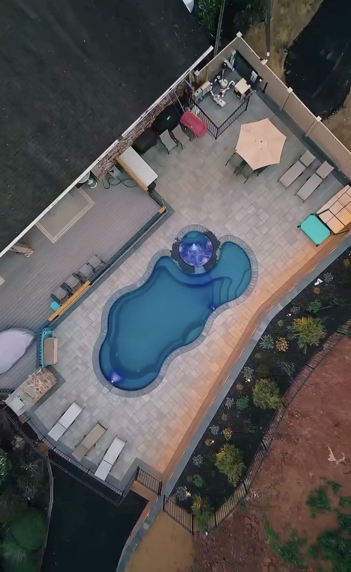 Aerial view of a backyard patio with a blue swimming pool, lounge chairs, and outdoor seating
