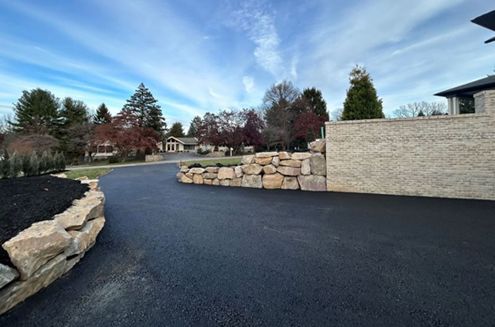 a driveway with a stone wall and a house in the background .