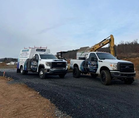 Two trucks are parked next to each other on a gravel road.