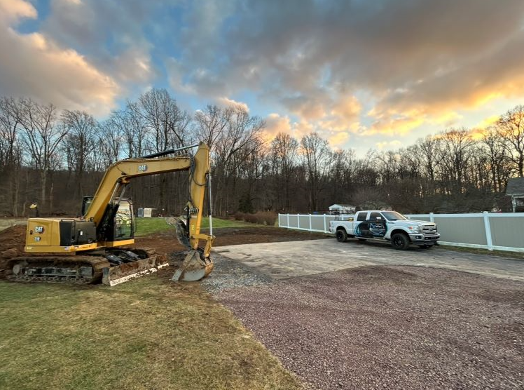 a yellow excavator and a white truck are parked in a driveway .
