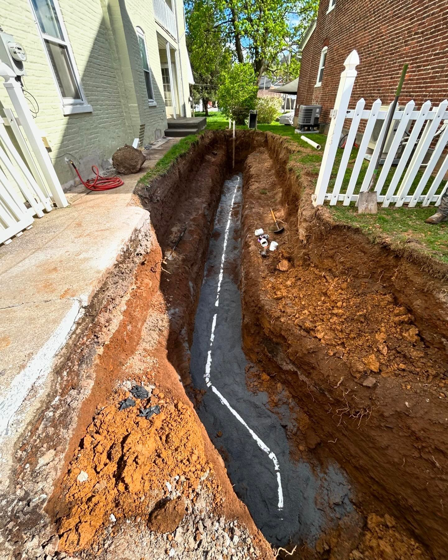 A drain pipe is being installed in a trench in front of a house.