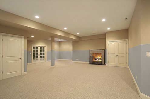 an empty basement with a fireplace and a carpeted floor .