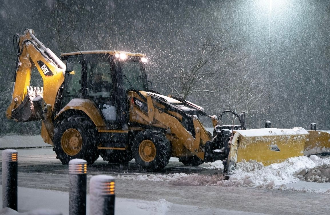 a yellow backhoe is clearing snow from a parking lot at night