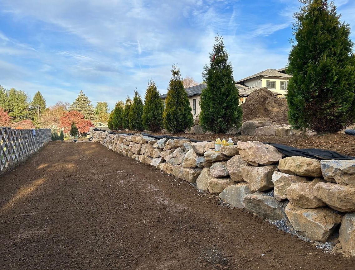 a stone wall with trees in the background and a house in the background