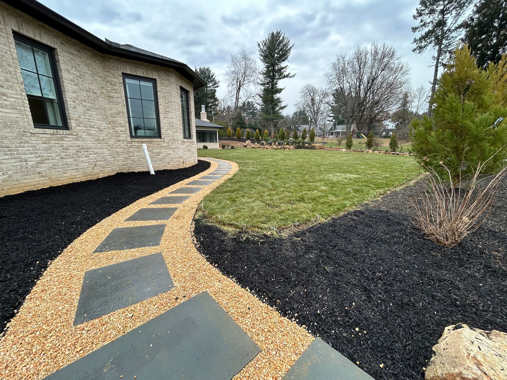 a walkway leading to a brick house with a lush green lawn .