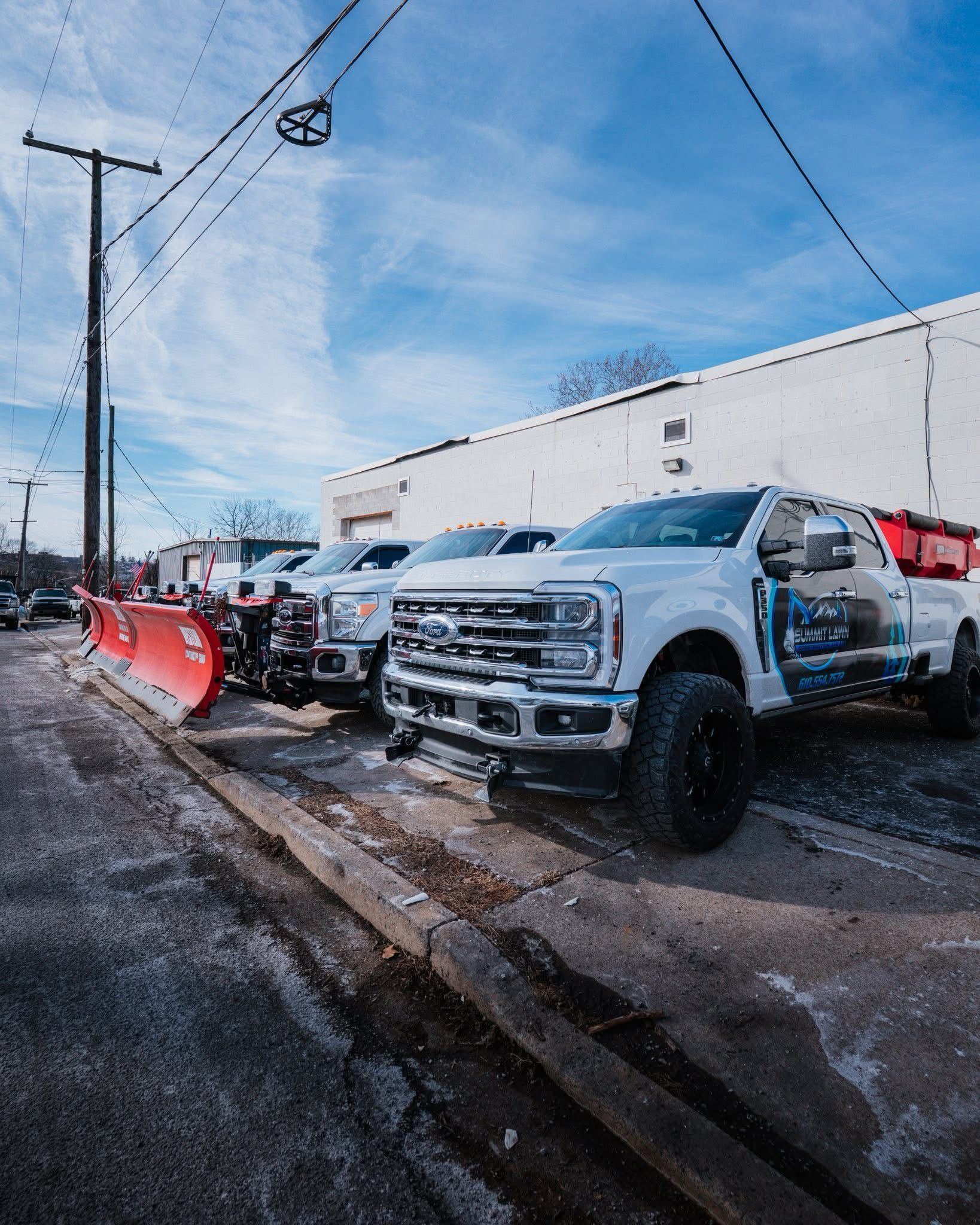 Snow plowing trucks parked on a street with a blue sky background.