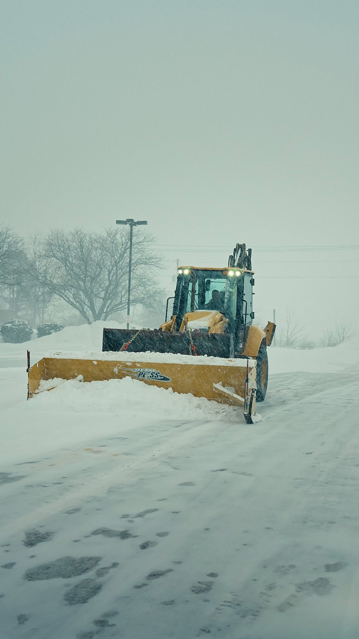 Yellow snowplow clearing snow on a road during a snowstorm.