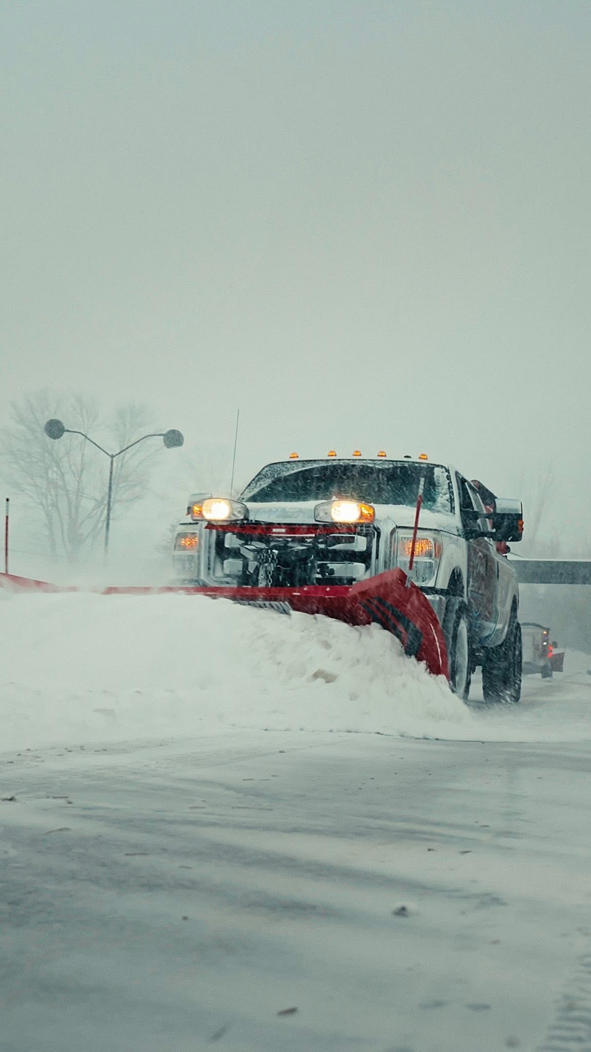 Snowplow truck clearing snow from a road during a snowstorm; white snow and gray sky.