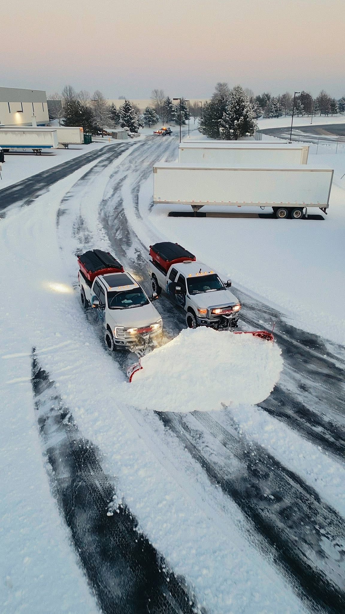 Snow plows clearing a snowy parking lot.