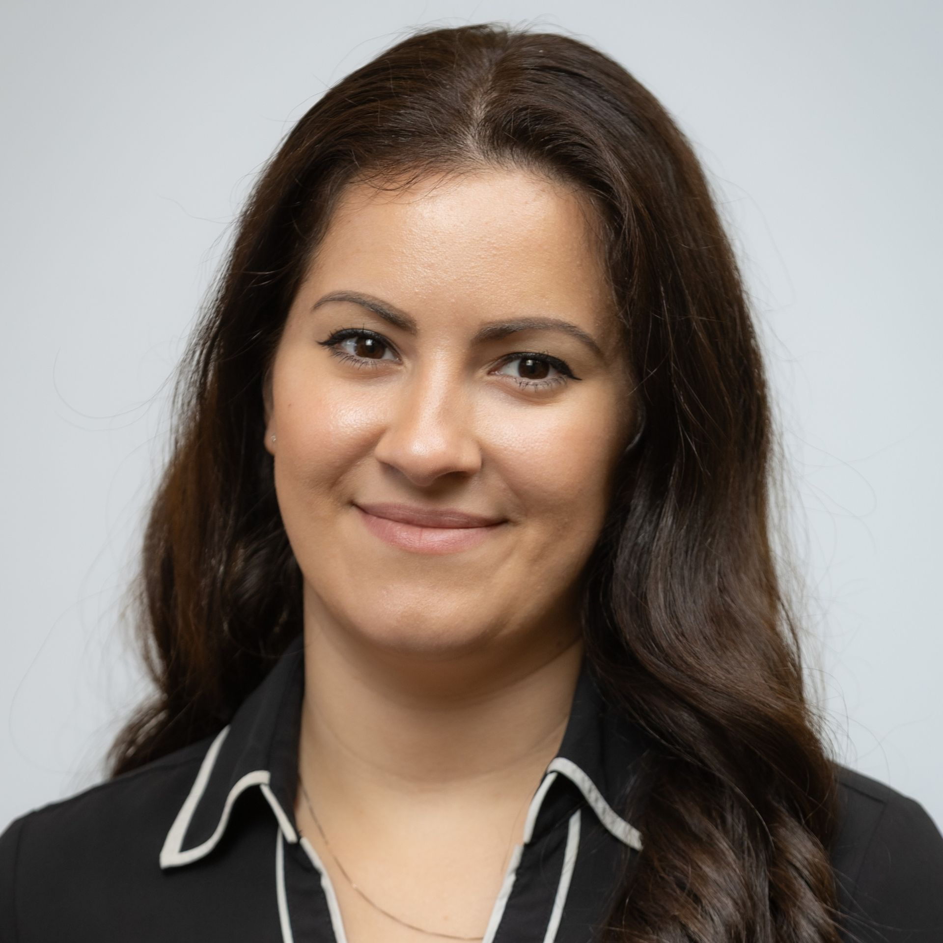 Woman with dark wavy hair wearing a black shirt with white trim, smiling, and looking at the camera.