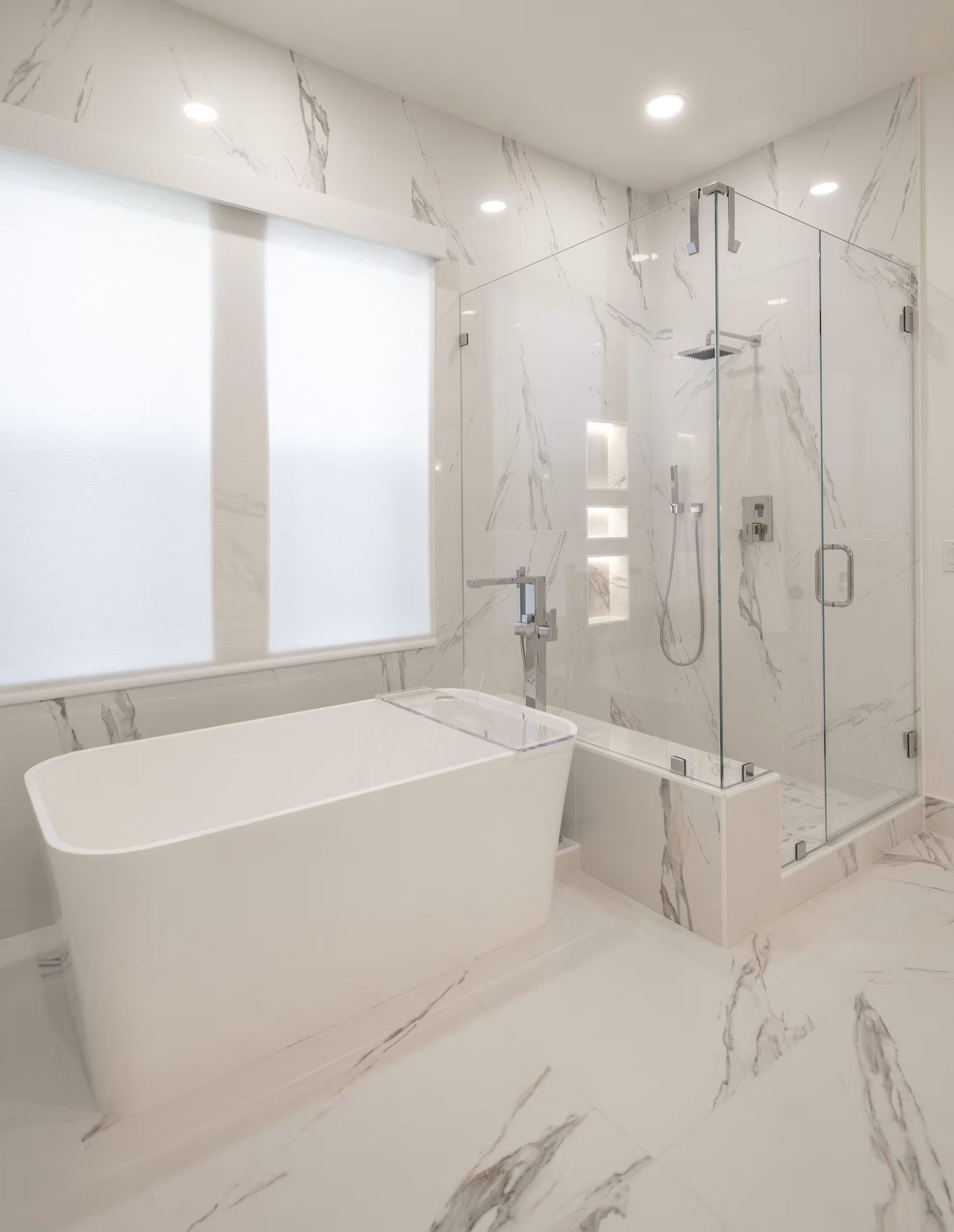 Bright modern bathroom with freestanding tub, glass shower, and white marble walls and floor