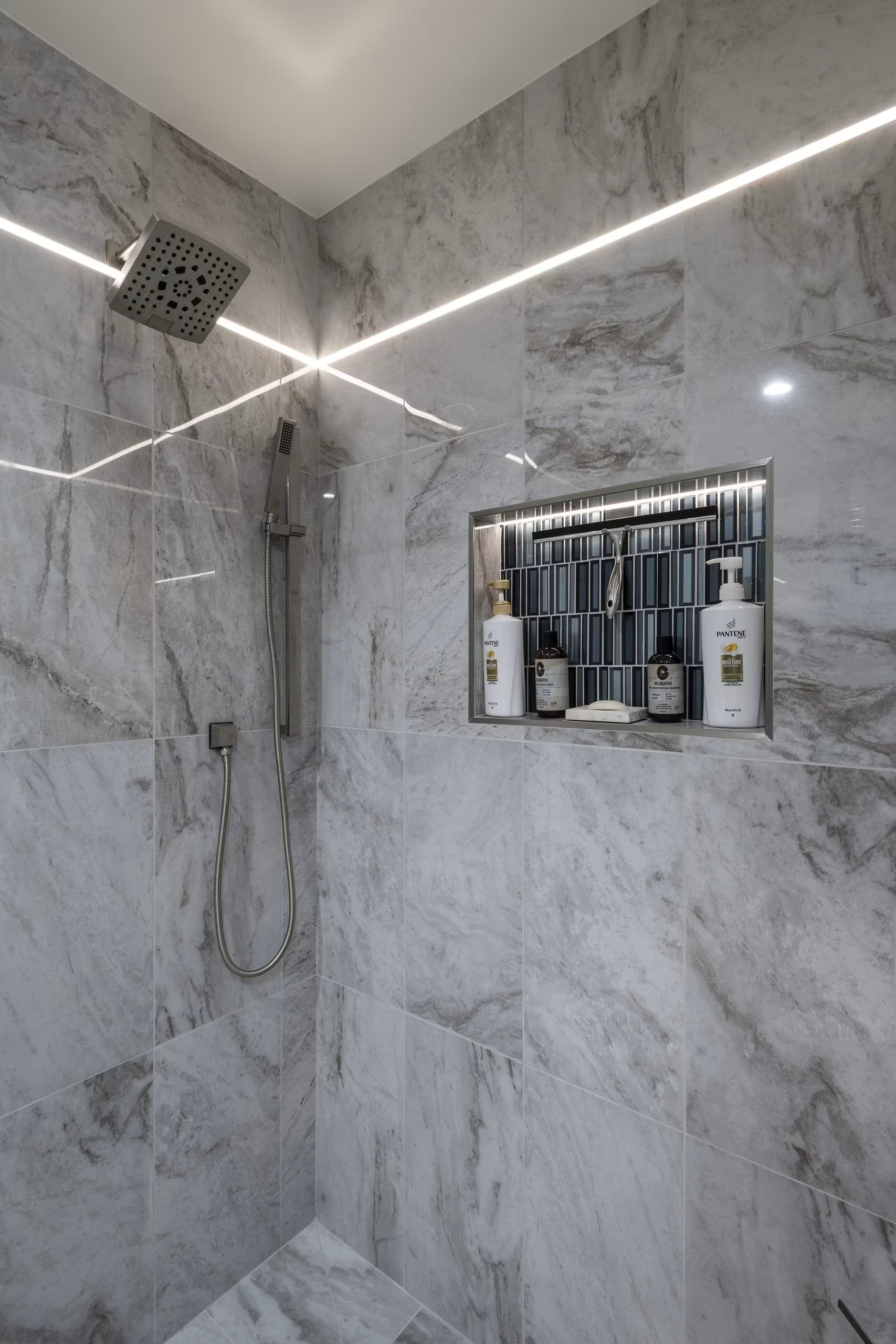 Modern marble-tiled shower with glass shelf, showerhead, and lit diagonal LED strips