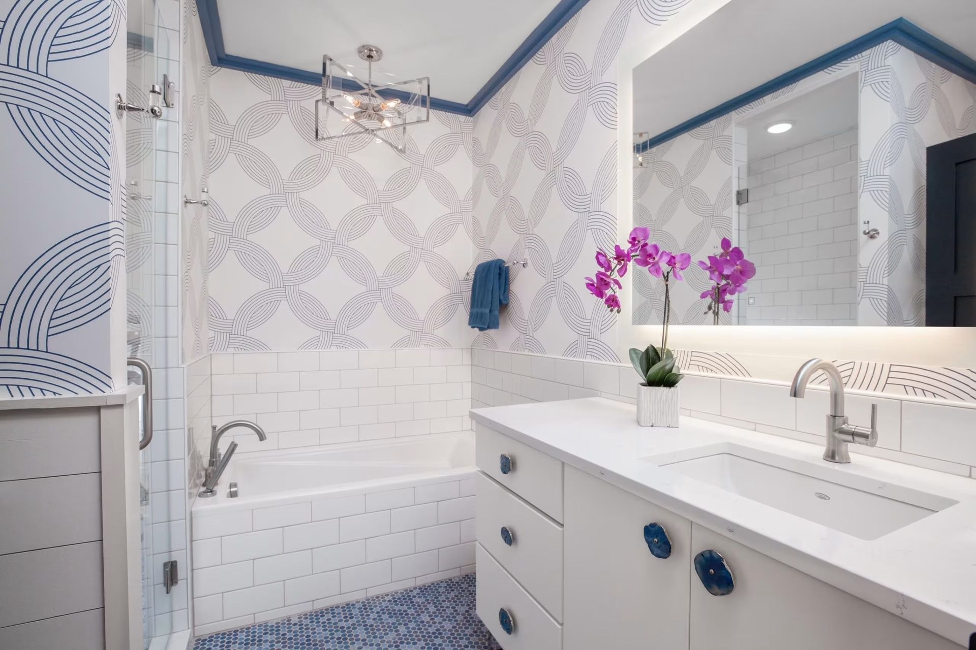 Bright white bathroom with blue accents, walk-in shower, vanity sink, mirror, and purple flowers