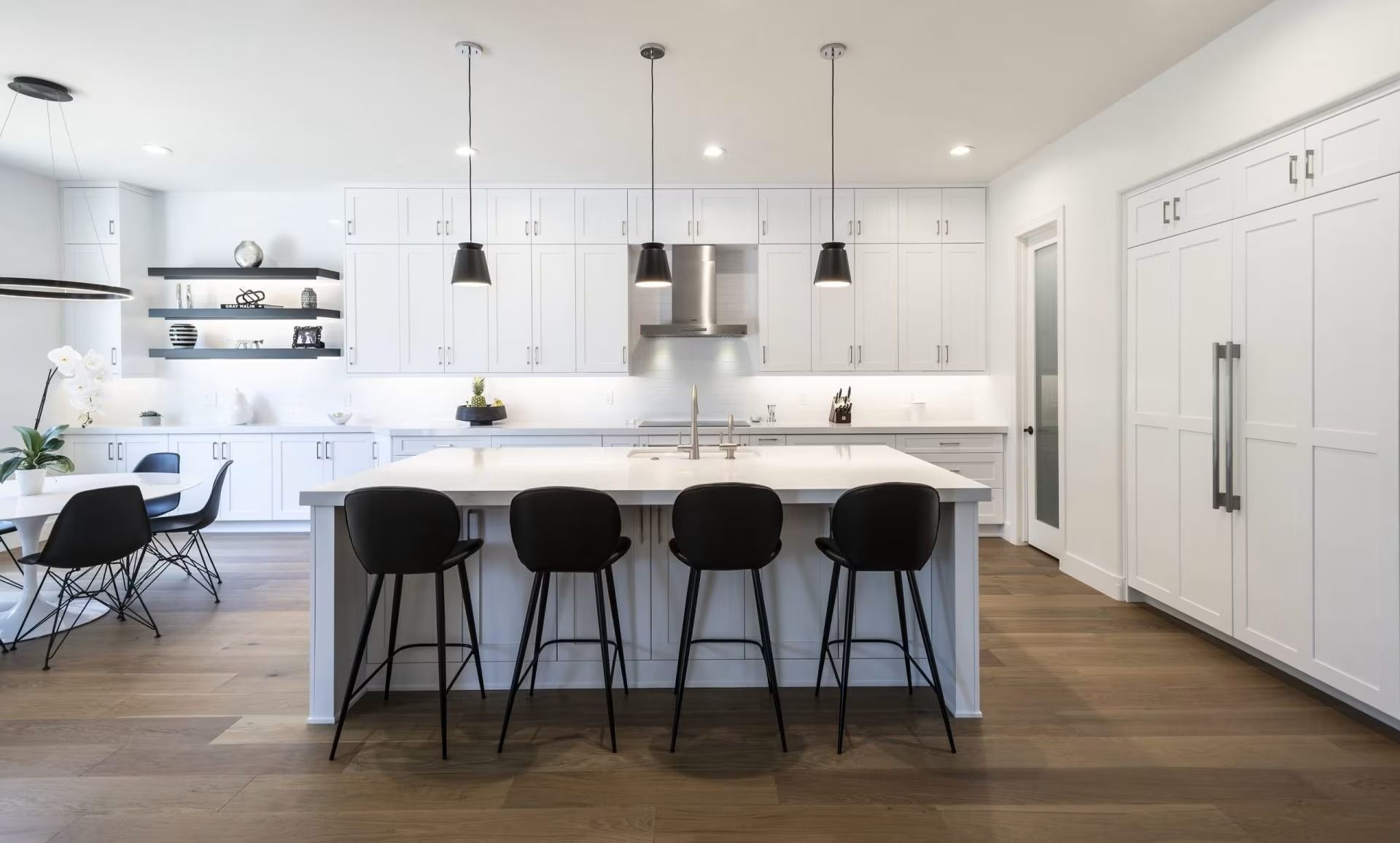 Bright modern white kitchen with island, black bar stools, pendant lights, and wood floors