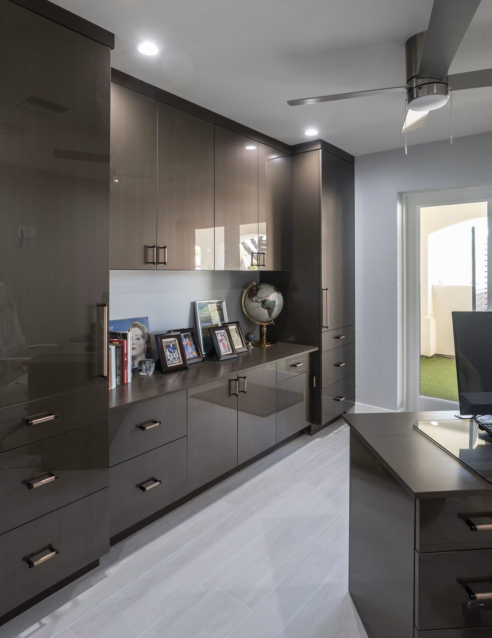 Modern kitchen with dark wood cabinets, silver countertop, and a doorway to a bright room.