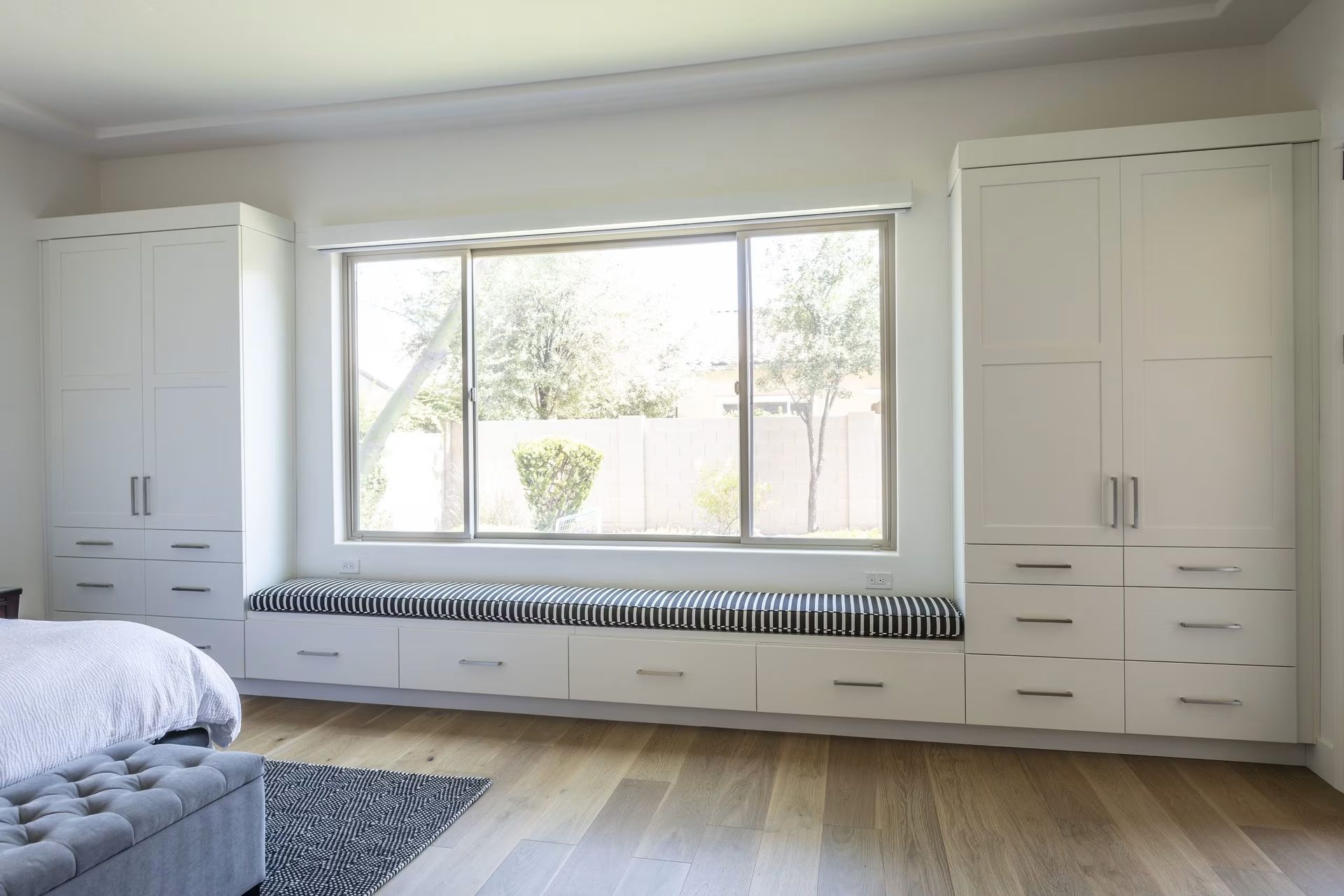 Bright bedroom with a large window, white built-in cabinets, and a bed in the corner.