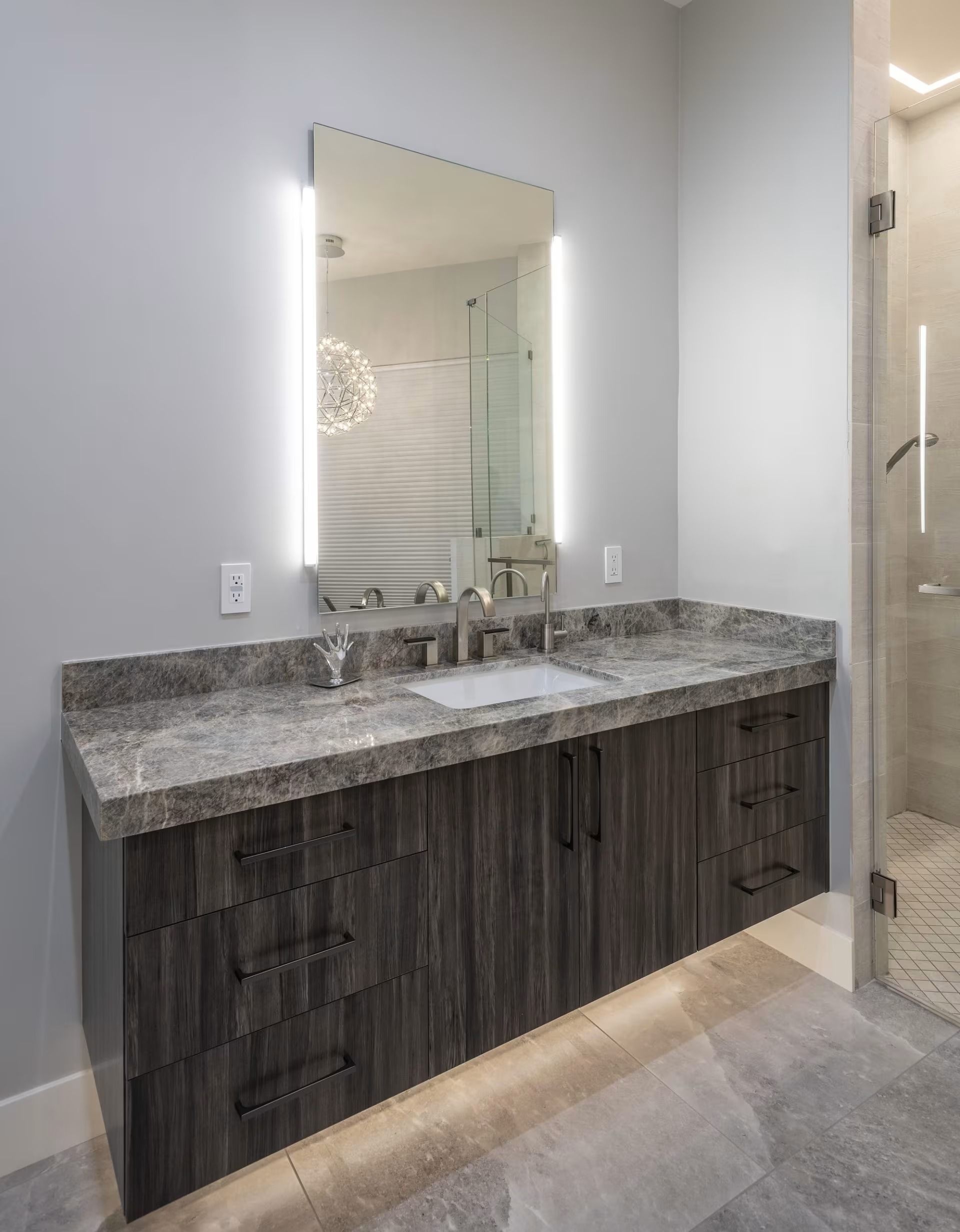 Modern bathroom vanity with gray stone countertop, dark wood cabinets, and mirror-lit wall sconces