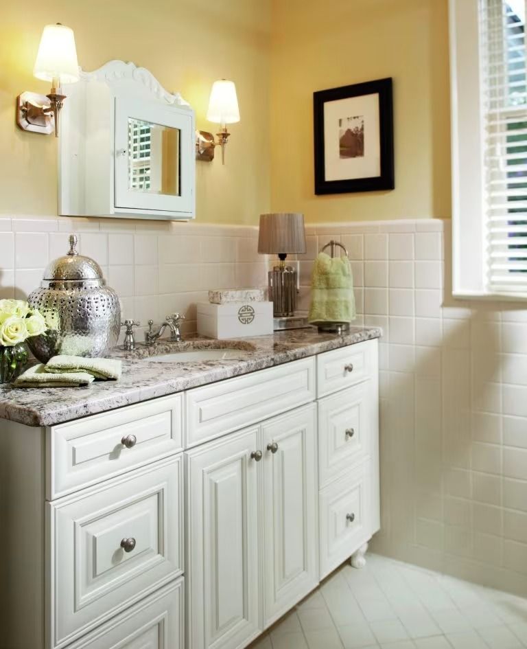 Elegant bathroom vanity with white cabinets, marble countertop, wall mirror, and sconce lights.