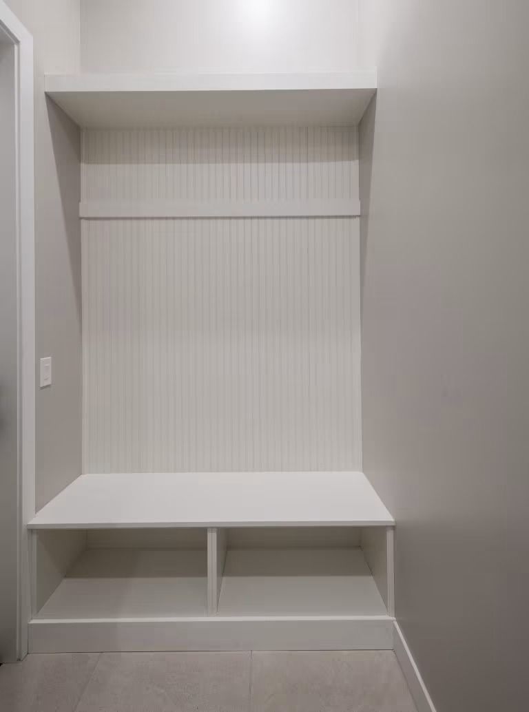 Built-in white closet nook with shelves, a bench seat, and lower storage cubbies