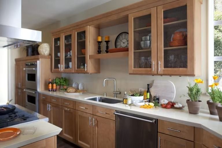 Modern kitchen with wood cabinets, white countertops, stainless appliances, and potted flowers on the counter